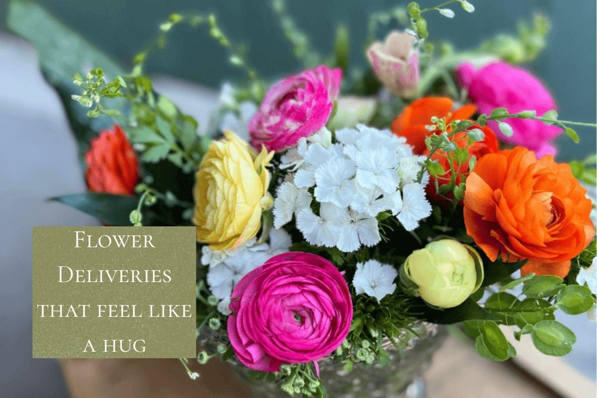 Bright bouquet of pink, orange, yellow ranunculus and white dianthus with text reading Flowers that feel like a hug